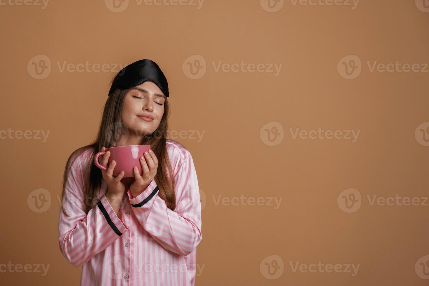 Pink pajama,. with cup of drink. Young pretty woman is against background in the studio photo