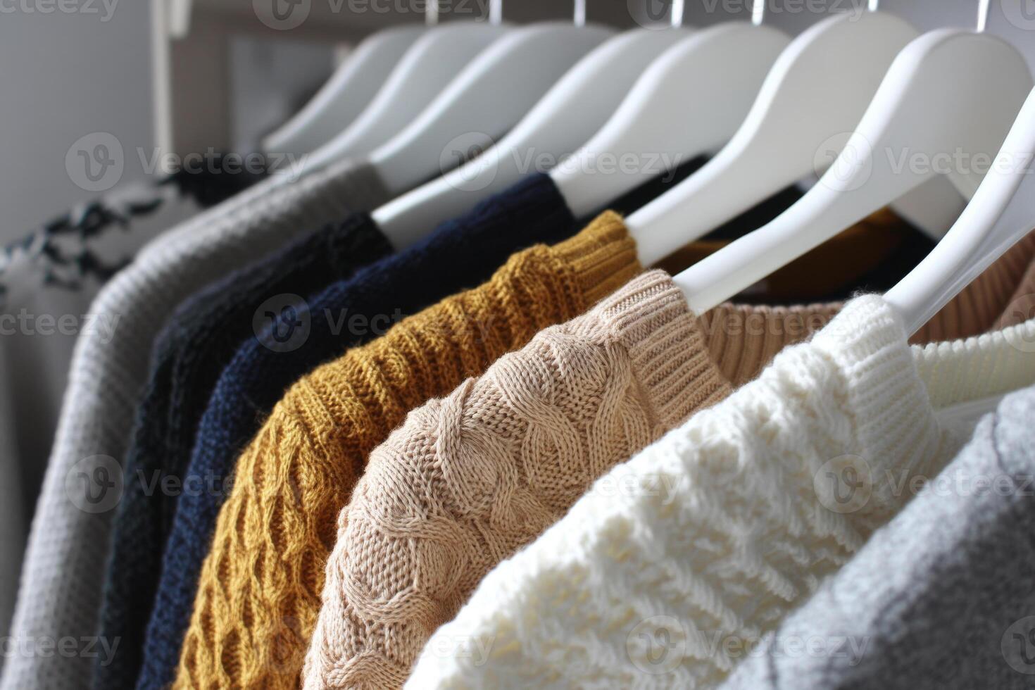 Sweaters hanging on white hangers in wardrobe photo
