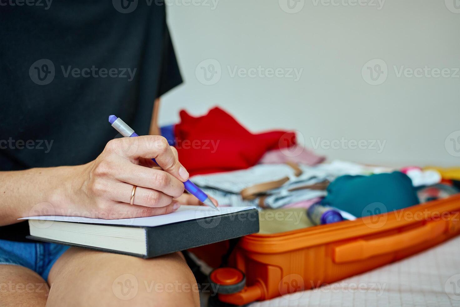 Woman preparing for travel, packing suitcase with clothes and checking travel packing list. Concept of holiday and vacation planning photo