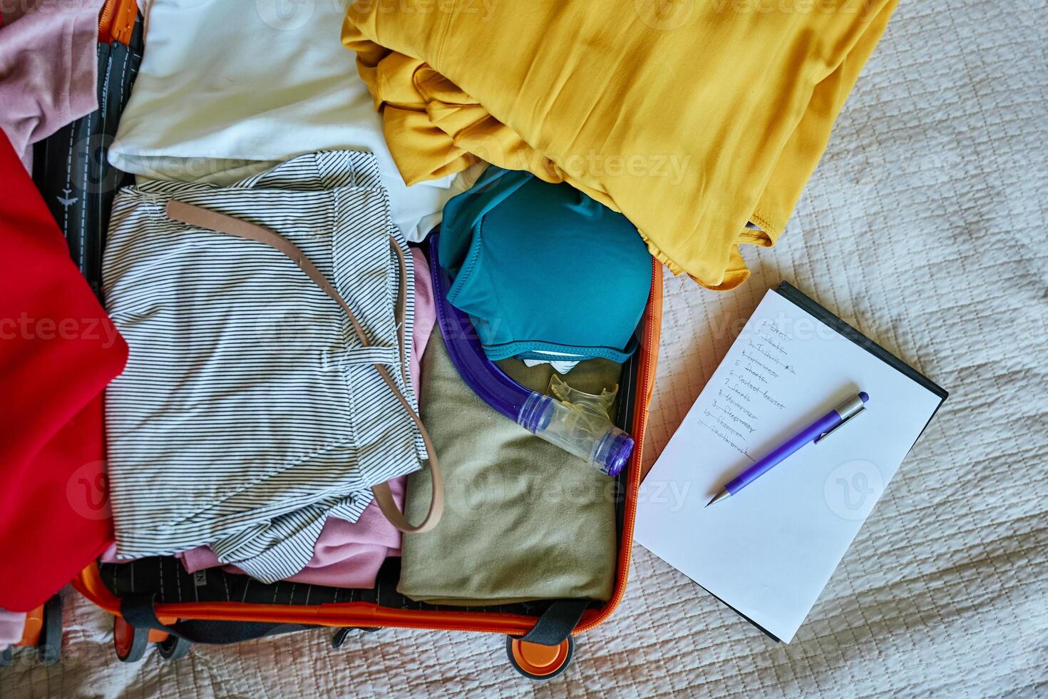 Handwritten checklist and pen on clothes packed into suitcase. Preparing for travel. Holiday and vacation planning photo