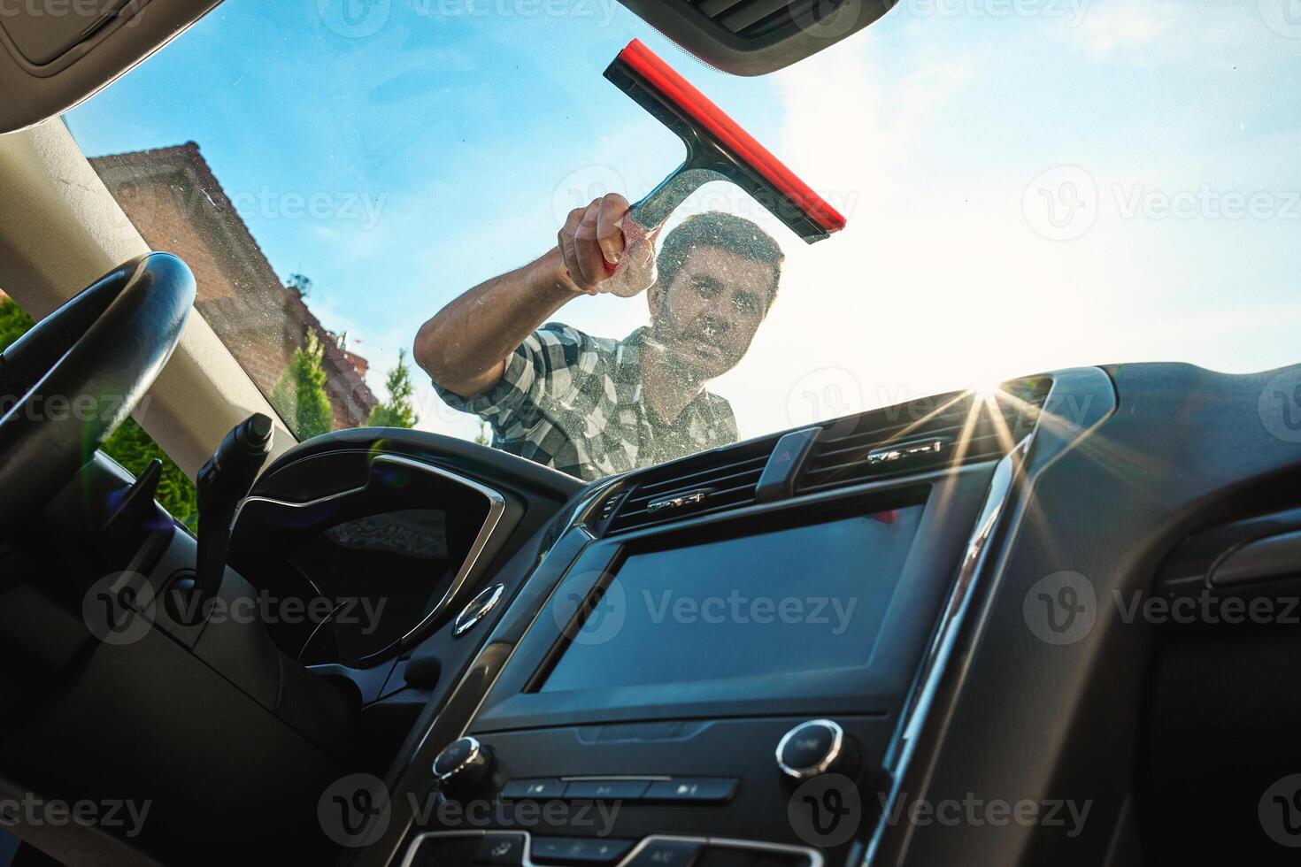 Man cleaning car windshield with squeegee, view from inside photo