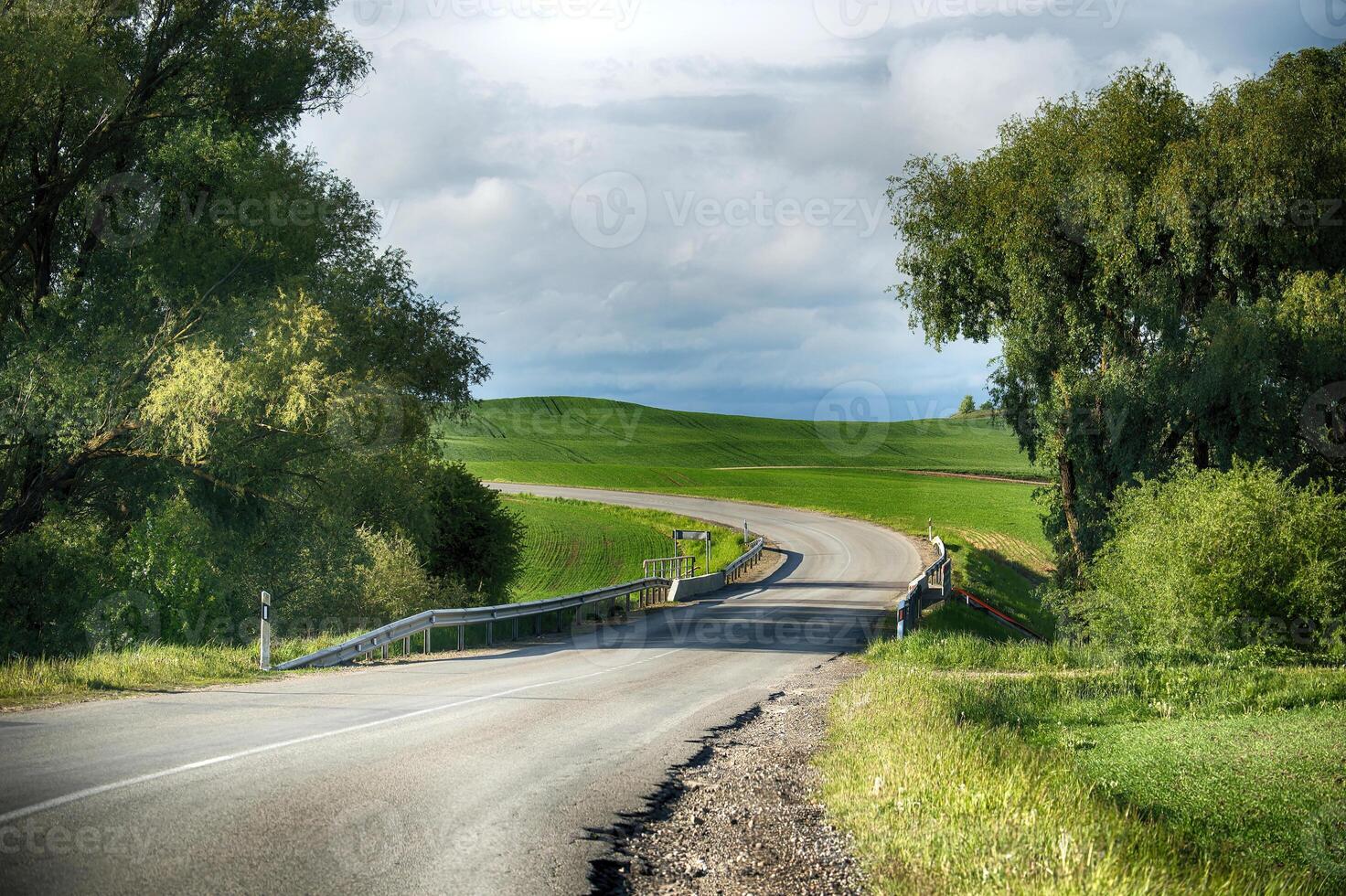 A beautiful winding road leading to a bright, green field on a sunny day in the countryside. photo