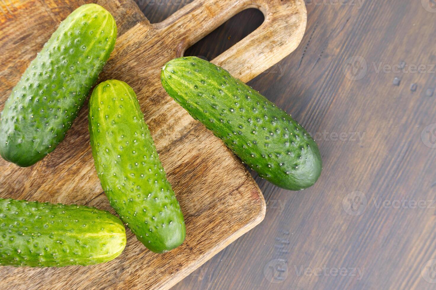 Fresh cucumbers lying on wooden cutting board photo