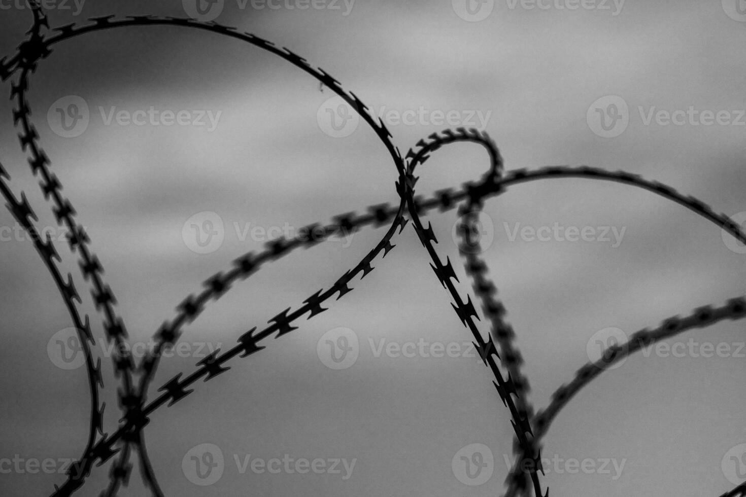 Fence with barbed wire in front of dark grey sky. Selective focus photo