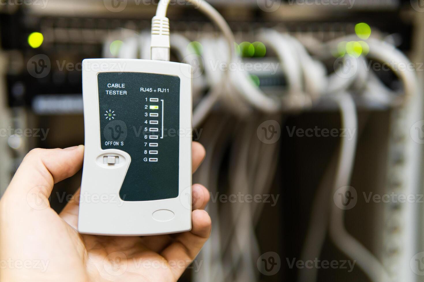 hand of system administrator or technician with tester tool for test network cables connected to patch panel of network gigabit switch in network data center. photo