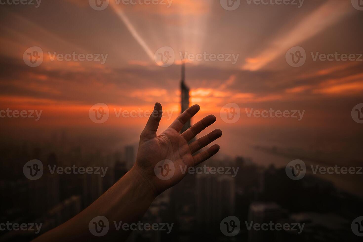 Silhouetted hand reaching toward city skyline at sunset photo