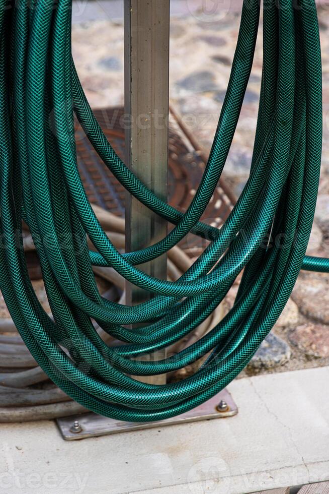 A thick green water hose is wrapped around a stand, Flexible garden hosepipe coiled on metal holder 05 photo