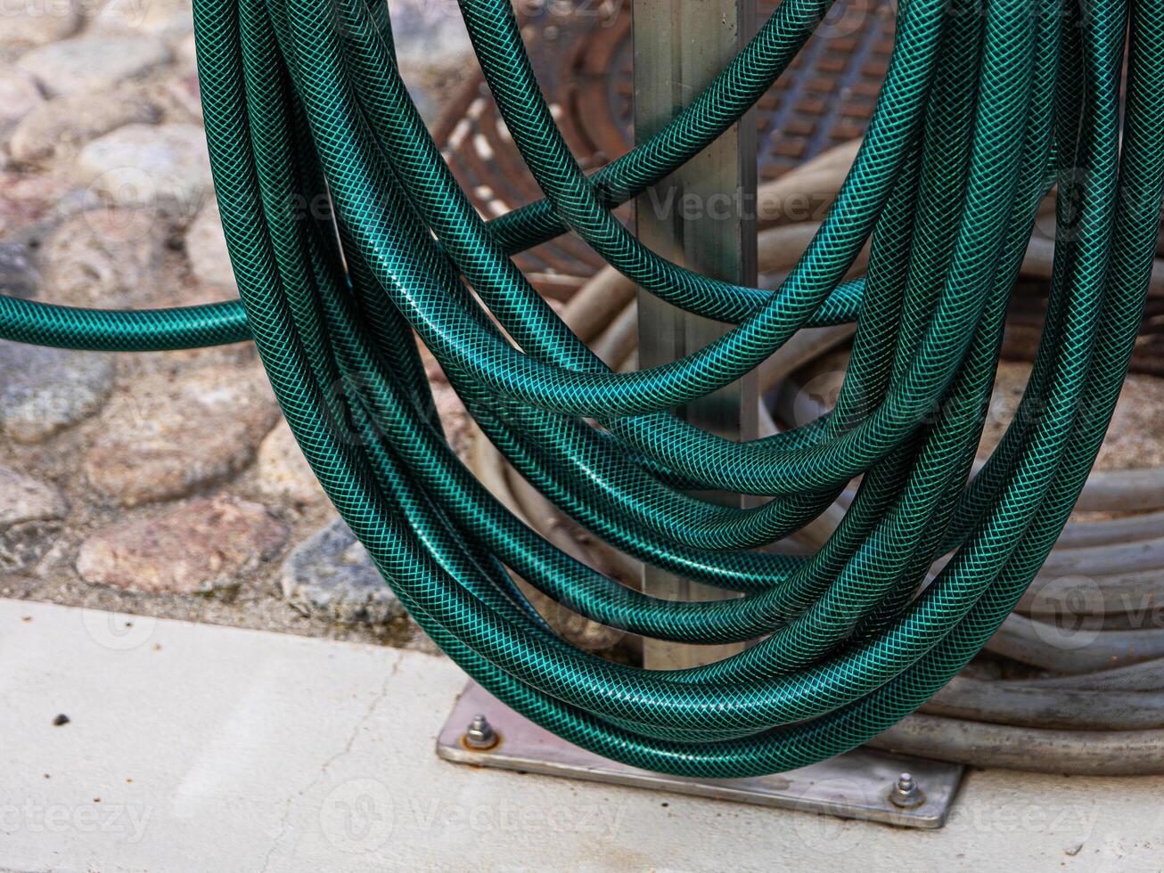 A thick green water hose is wrapped around a stand, Flexible garden hosepipe coiled on metal holder 01 photo