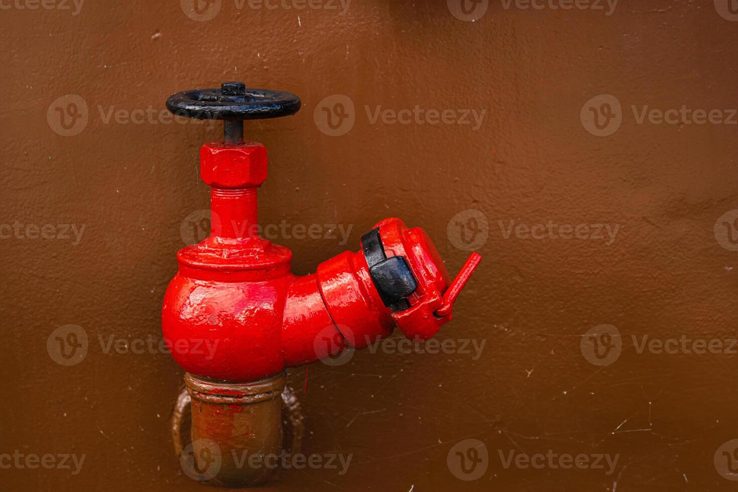 A vivid red industrial ship valve stands out against a clean brown metal wall. Big boat tap on rust painted hull surface 12 photo