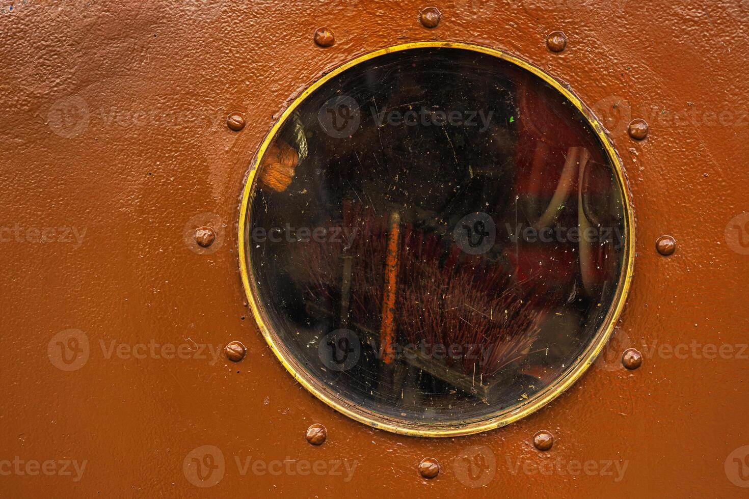 A detailed closeup of a round porthole with a protective glass on the brown painted old boat wall. Brooms are stored inside 26 photo