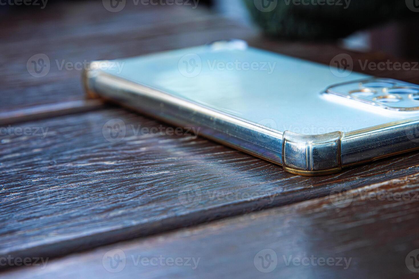 Closeup of the smartphone with silver body and a transparent protective case placed on a dark wooden table. Selective focus photo