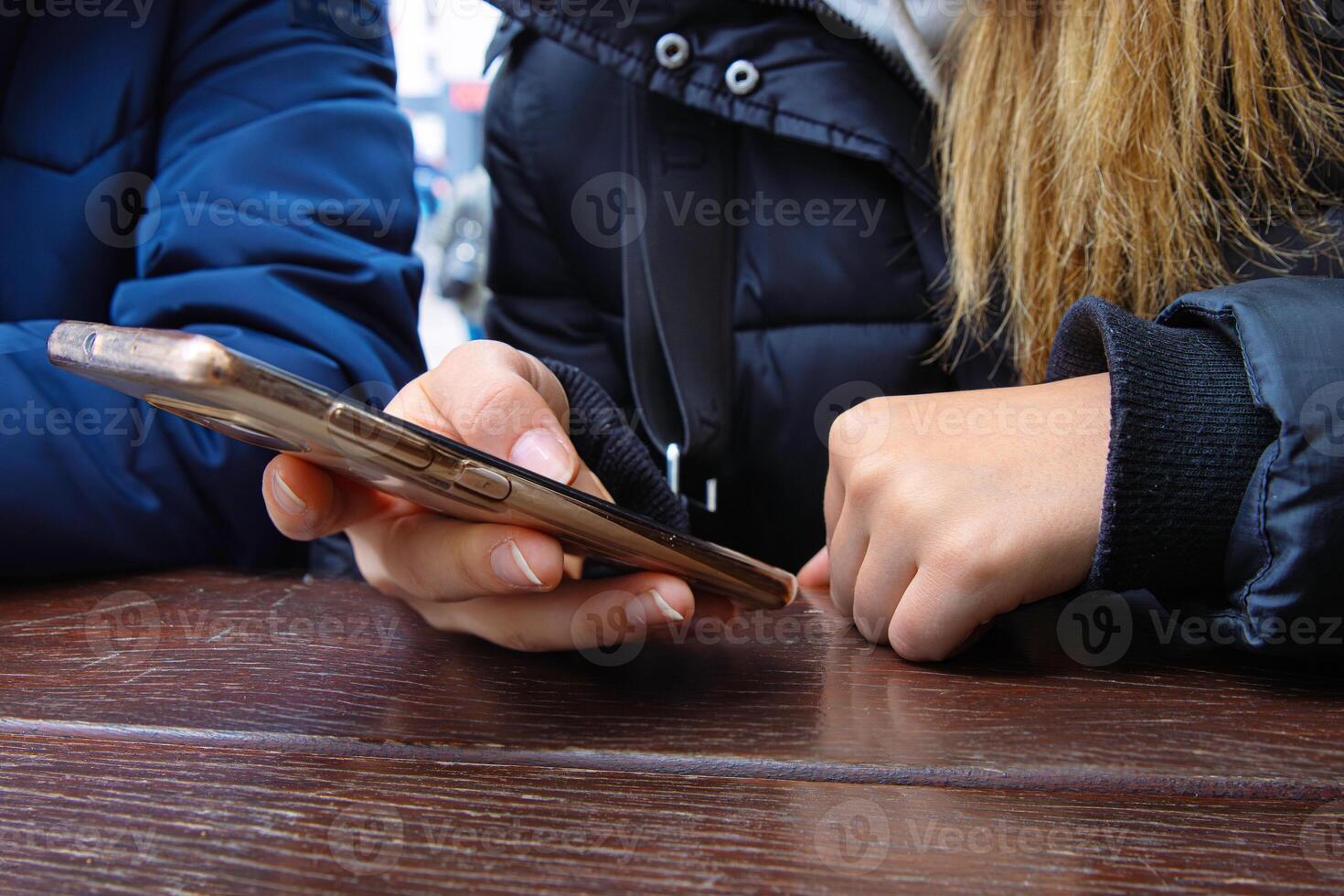Woman using a smartphone, actively scrolling on a touchscreen, while sitting at an outdoor cafe wooden table. Selective focus 10 photo