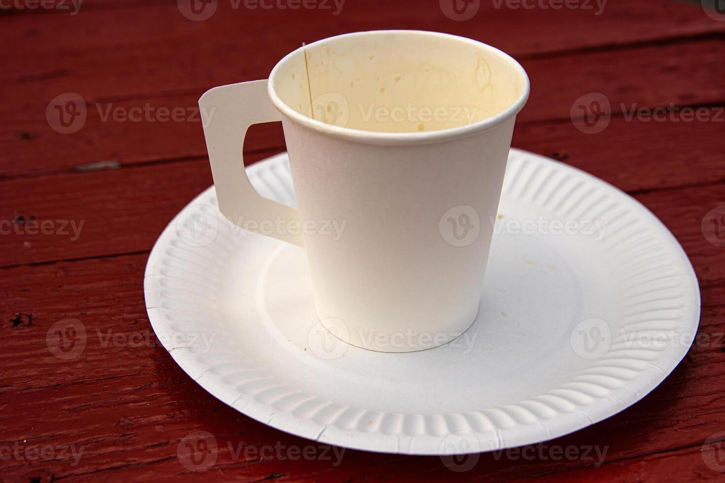 A white paper coffee cup with a handle placed on a white paper plate set on a rustic red wooden table in an outdoor cafe in Hamina, Finland 01 photo