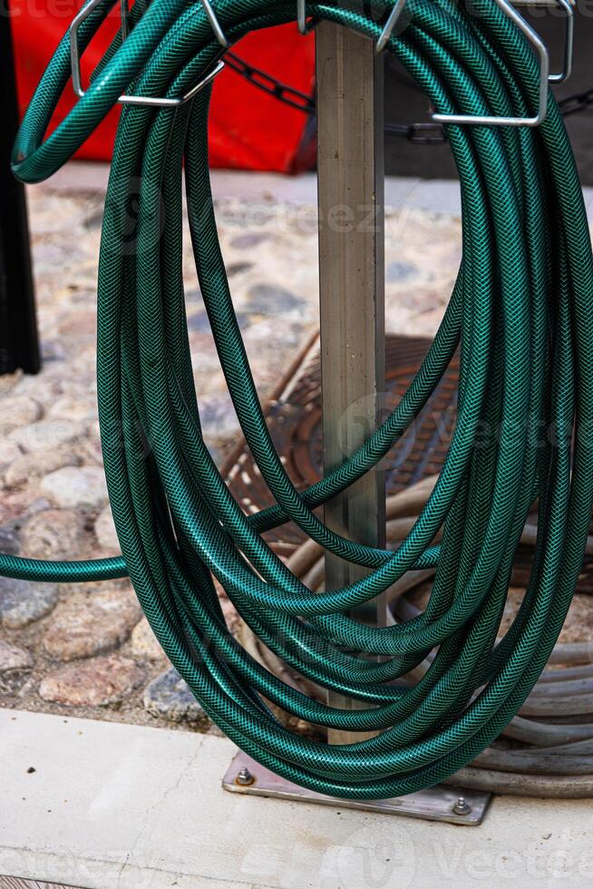 A thick green water hose is wrapped around a stand, Flexible garden hosepipe coiled on metal holder 19 photo