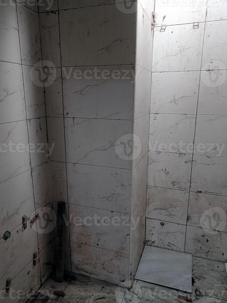 Bathroom corner with white tile and drain shows worn, unkempt state of being as grout is dirty and floor is stained, creating feeling of neglect photo