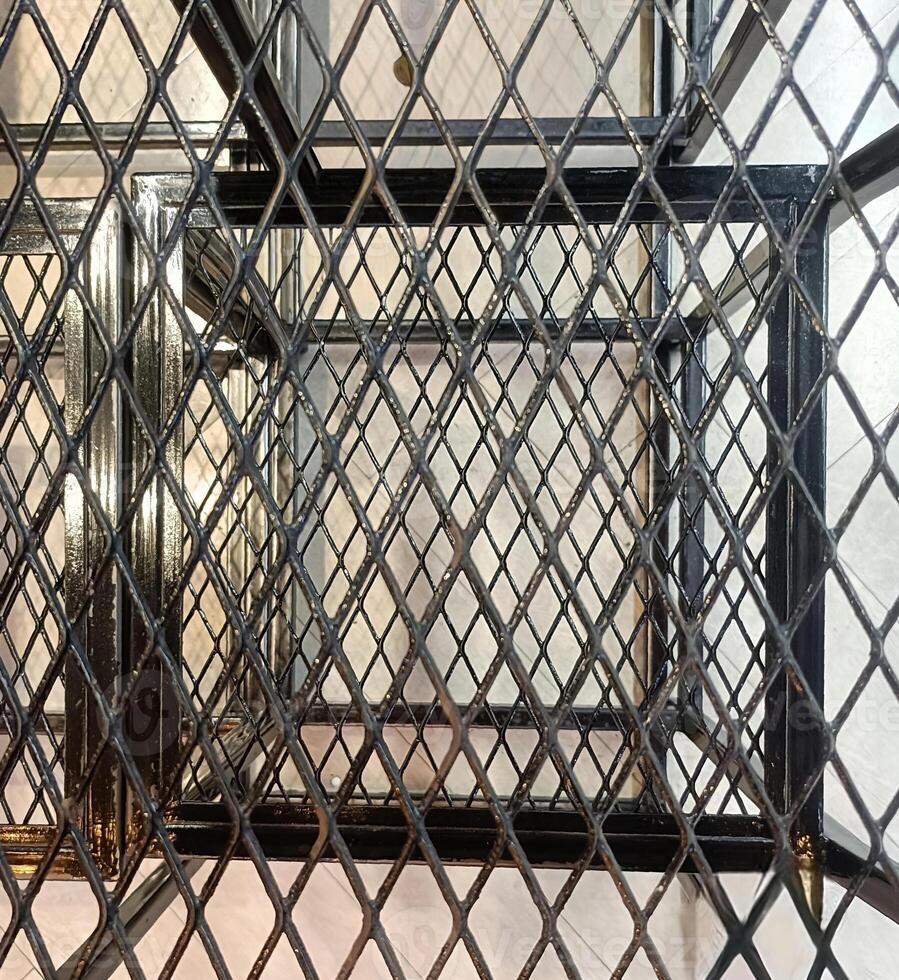 Geometric pattern of intersecting metal grids creates complex, industrial design. black metal framework contrasts with light background, forming striking visual effect photo