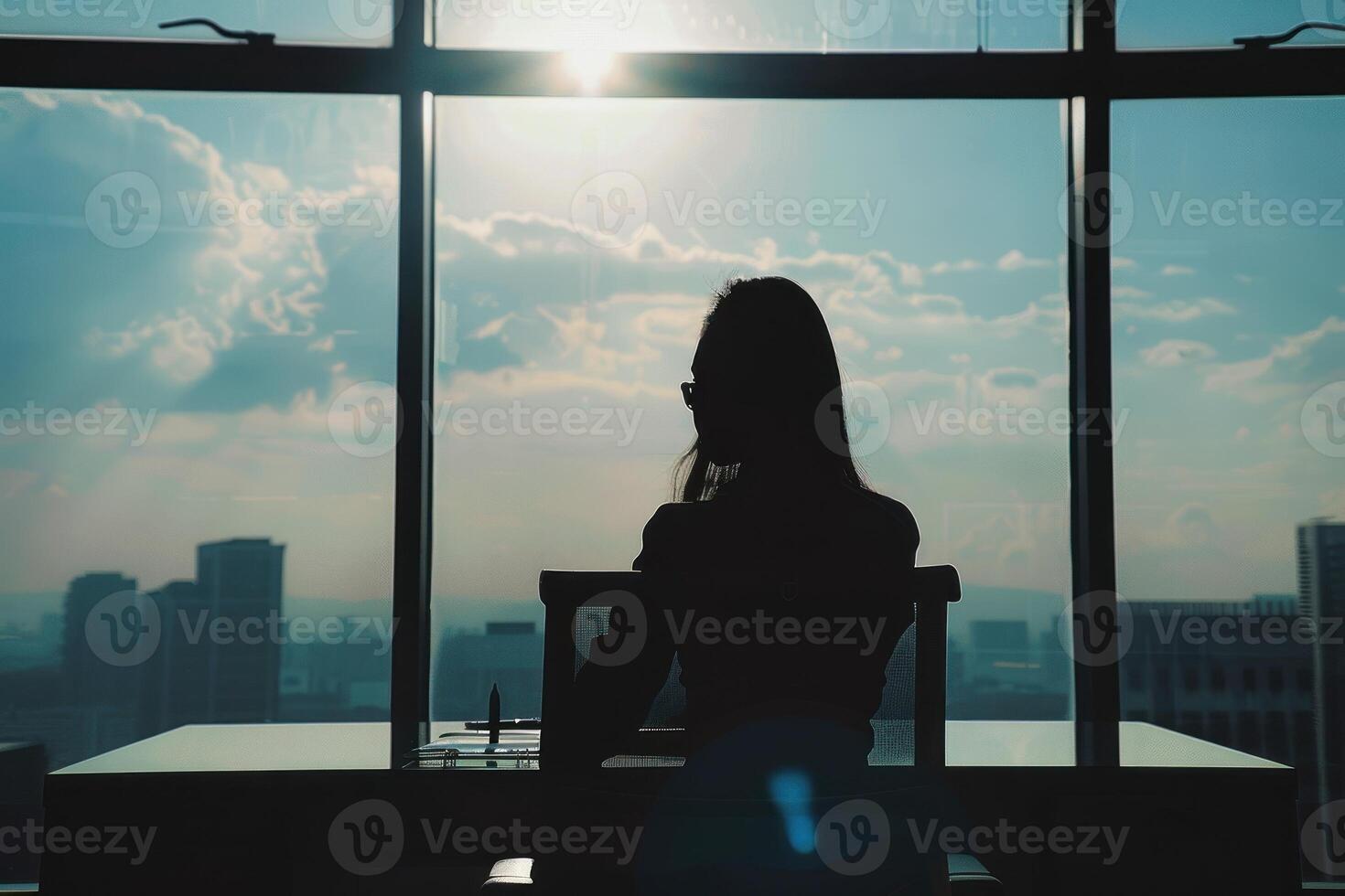 A woman sitting at a desk looking out a window photo