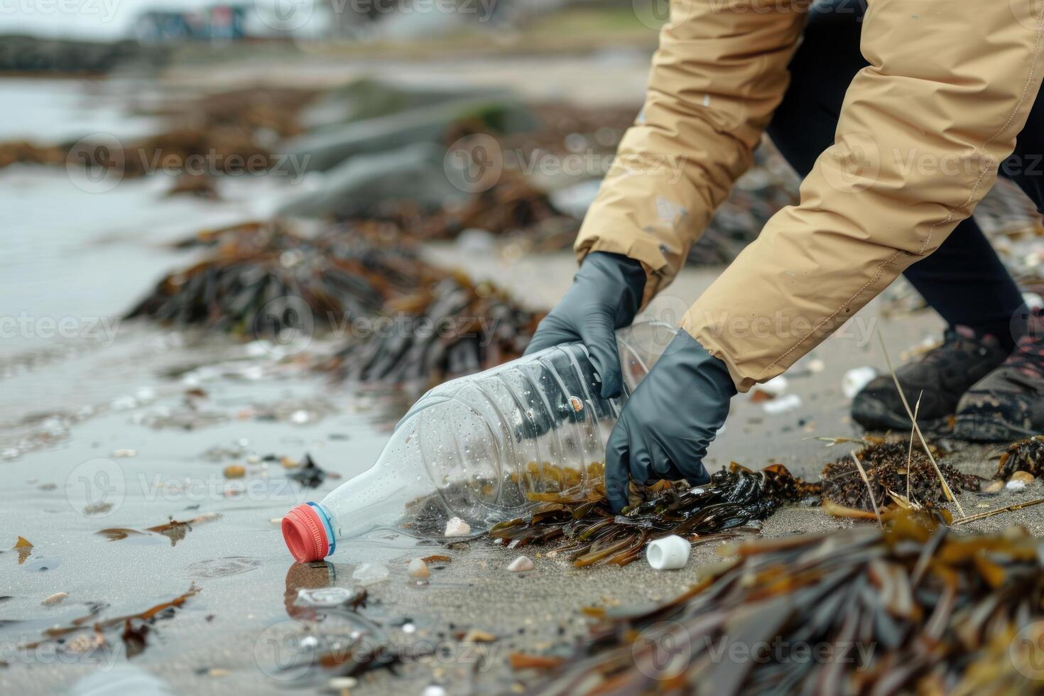 A person in gloves picking up a plastic bottle from the beach photo