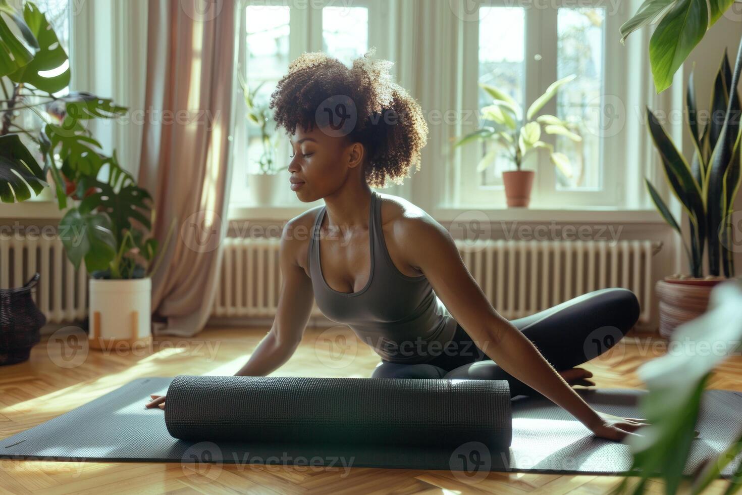 A woman is sitting on a yoga mat in front of a window photo