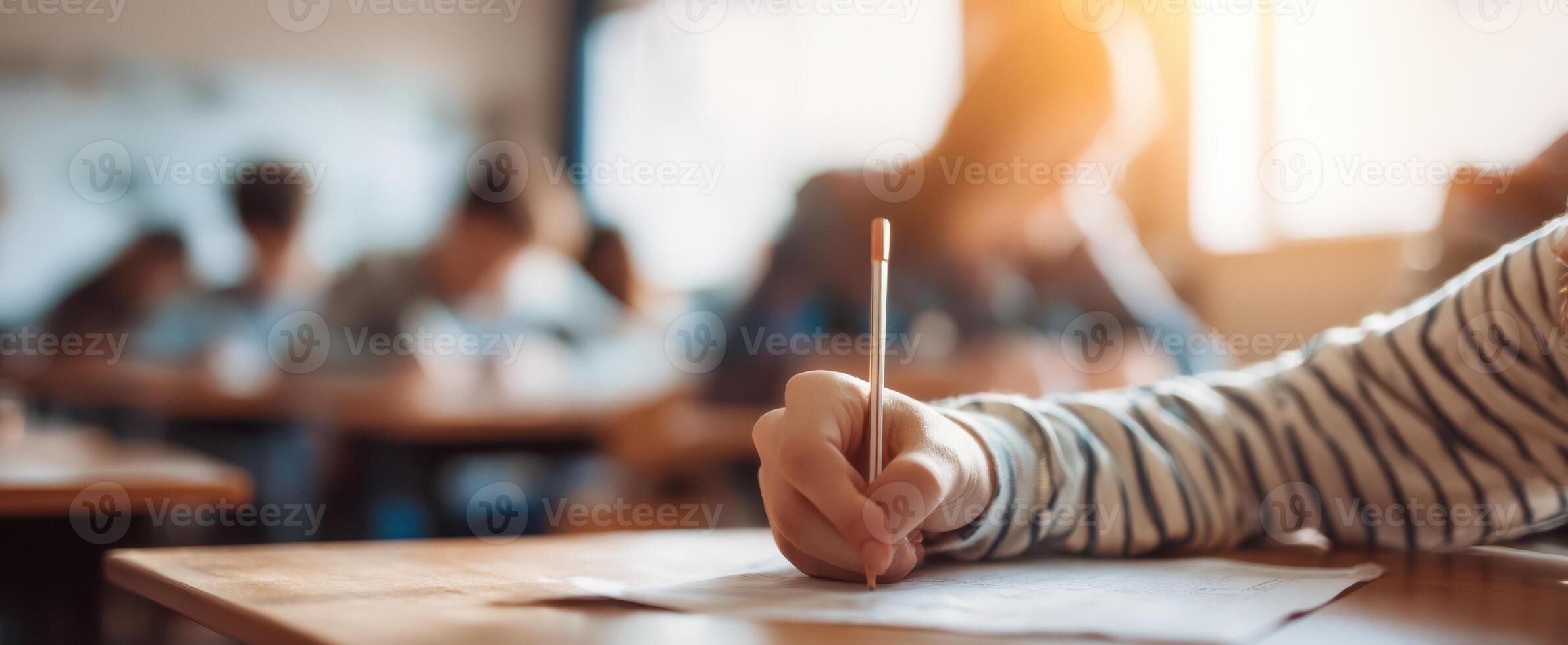 The student focused on writing during a classroom exam with peers around. photo