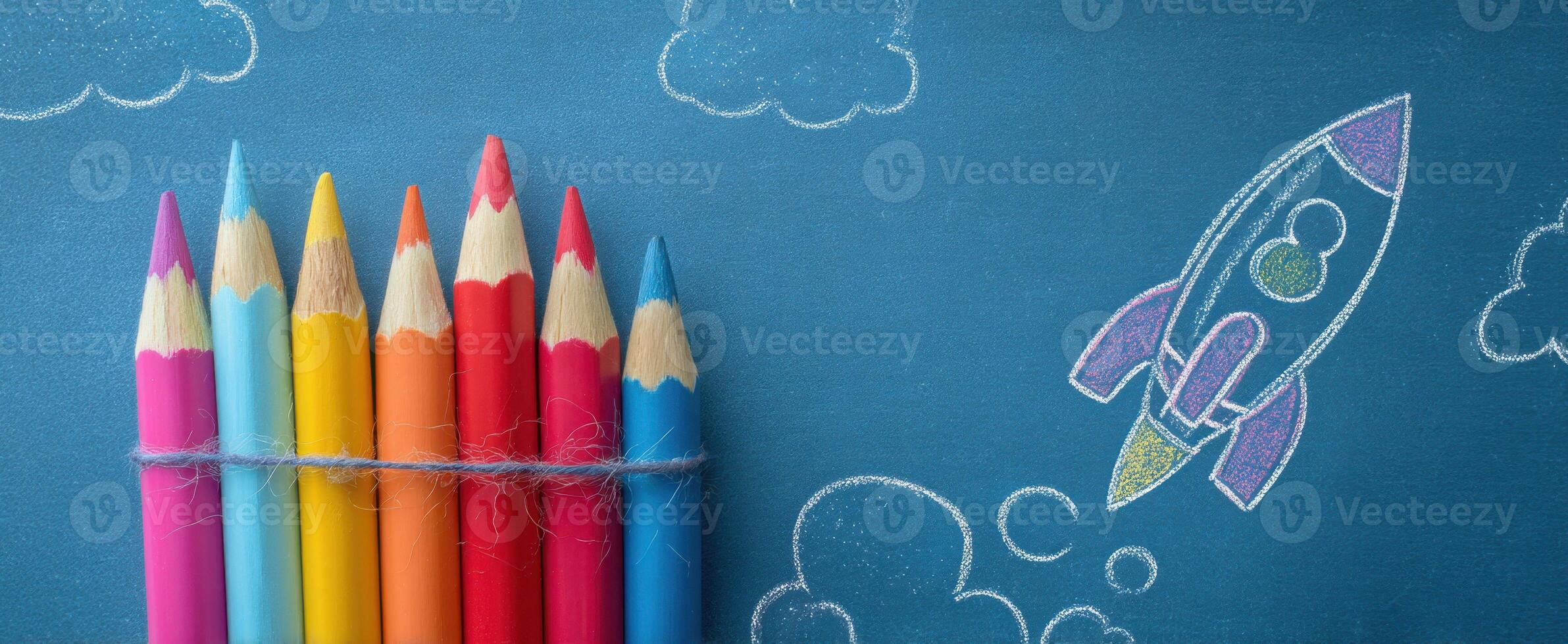 The colorful pencils and chalk rocket against a bright blue background. photo