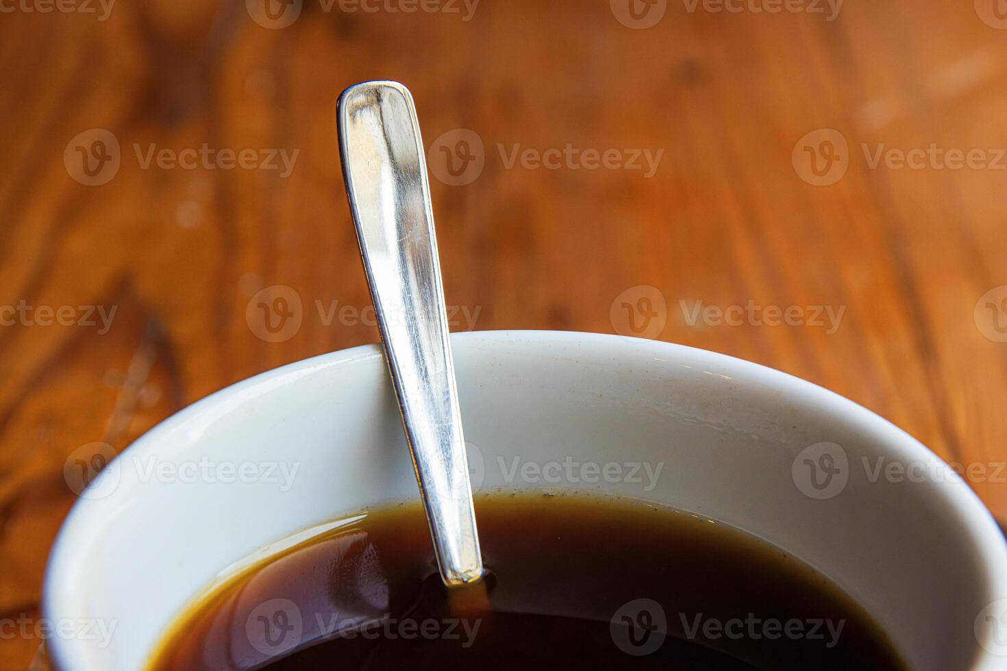 A closeup of a white ceramic cup filled with black coffee, with a metal spoon inside, placed on a rustic wooden table.Soft focus 09 photo