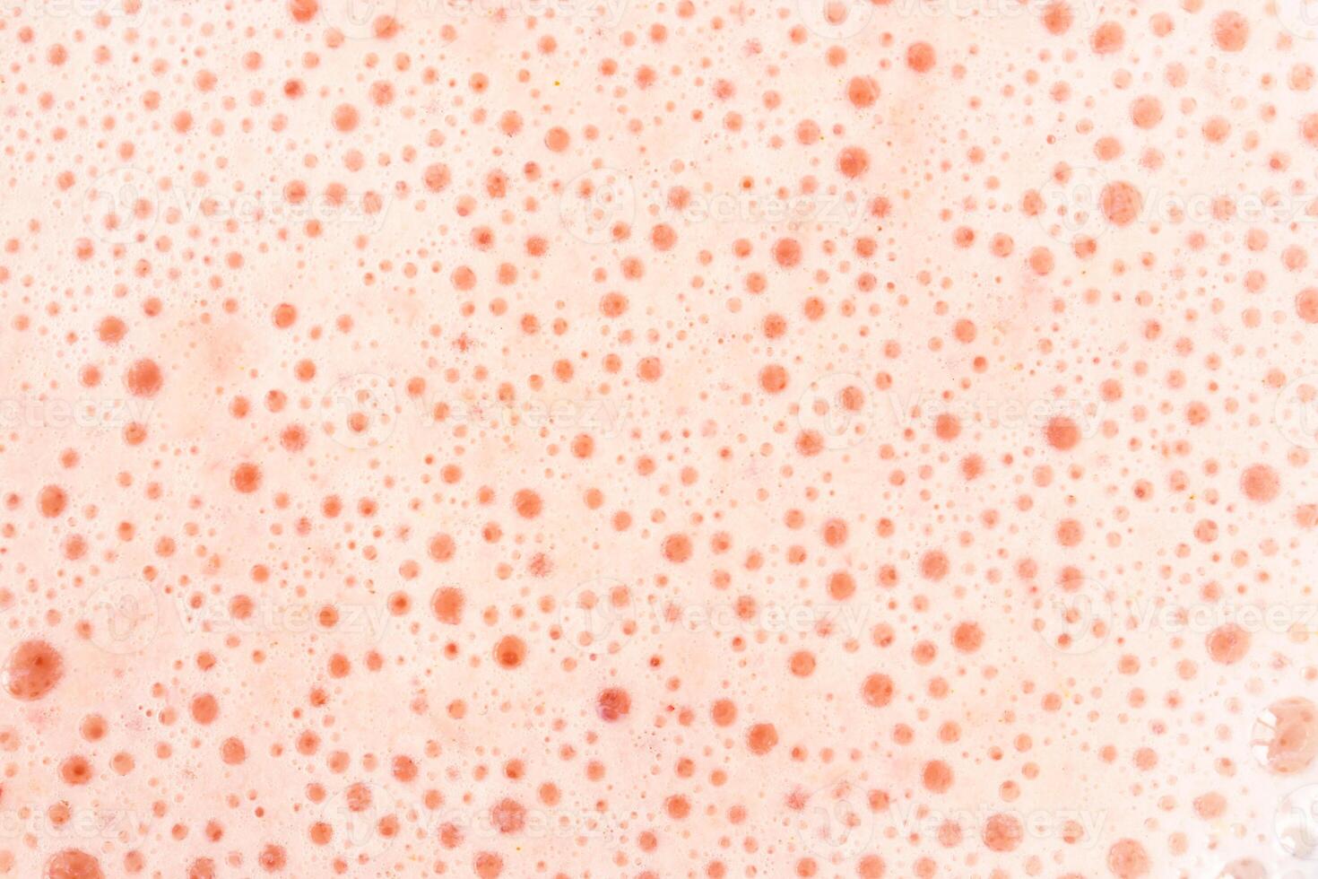 Foam texture with small bubbles on a light pink background. Close up macro view of liquid surface with air bubbles. Smooth beverage background. photo