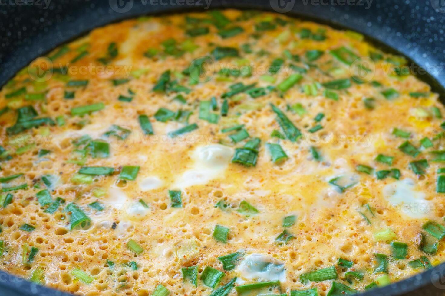 Green onion omelet in frying pan, a breakfast food idea. Macro shot of fresh eggs and herbs prepared for healthy meal concept. photo