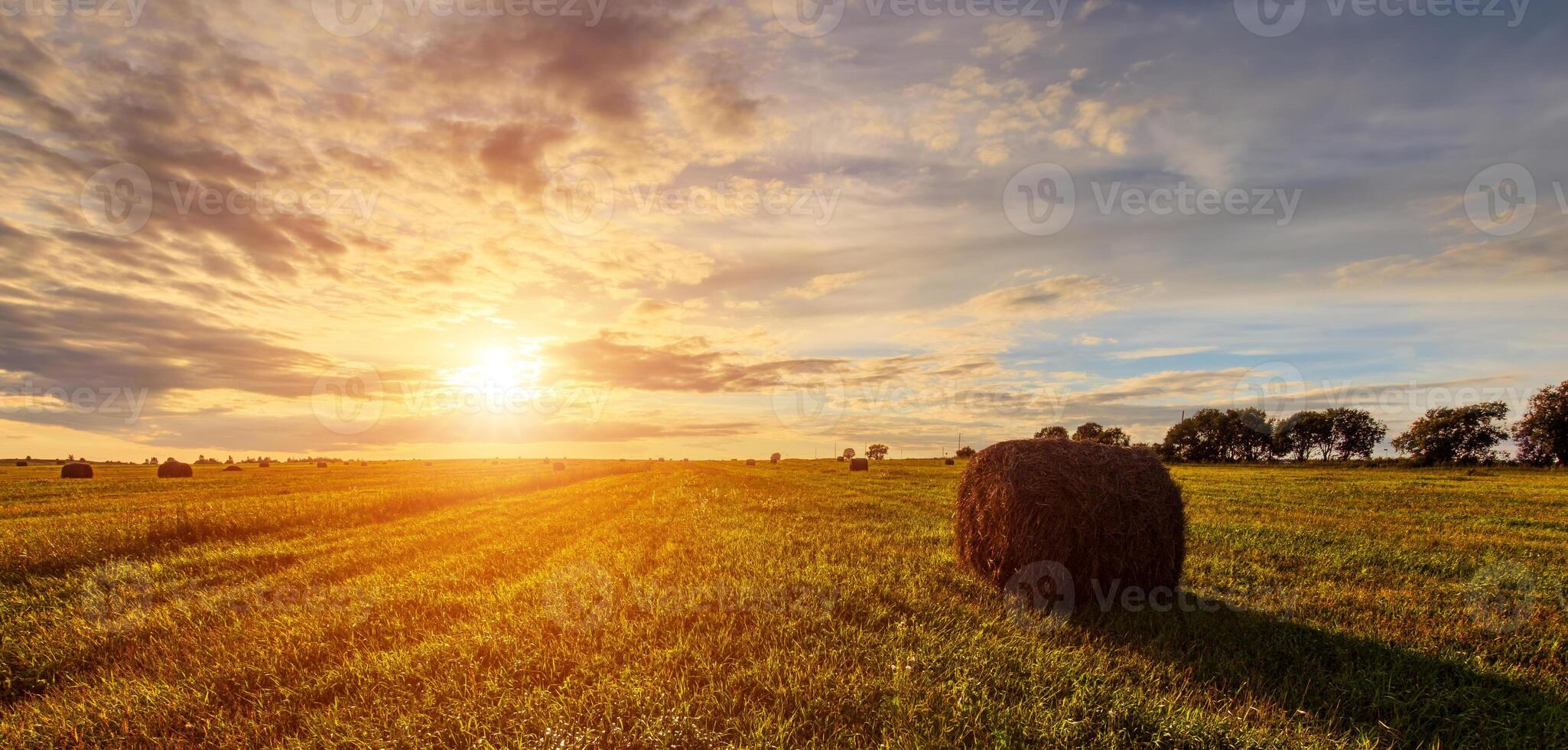 Scenic sunset or dawn over hay bales in a field. Golden light bathes the landscape, creating a tranquil scene. For agriculture, travel and inspiring greeting card designs. photo