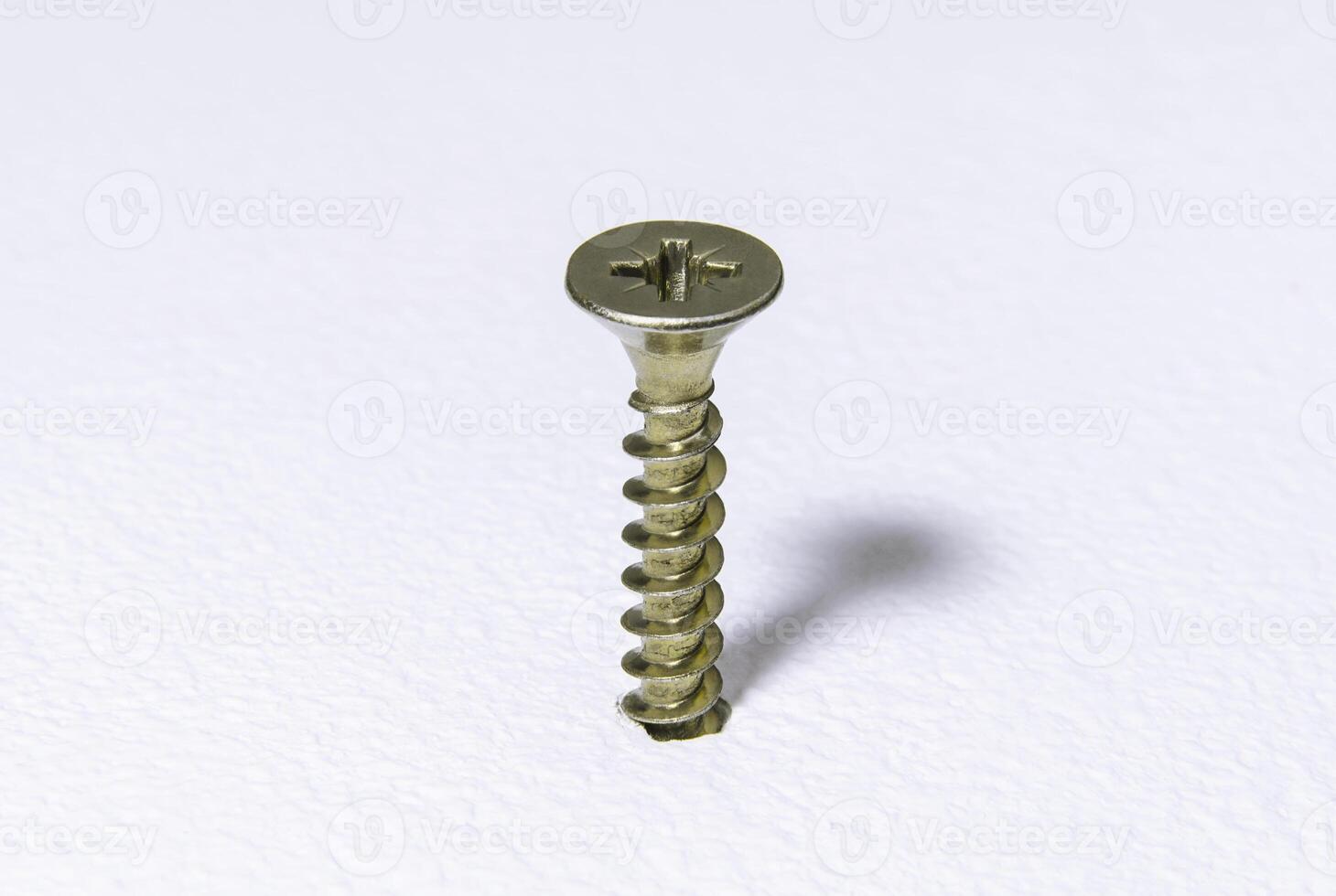 Shiny steel screw screwed into a white rough surface photo