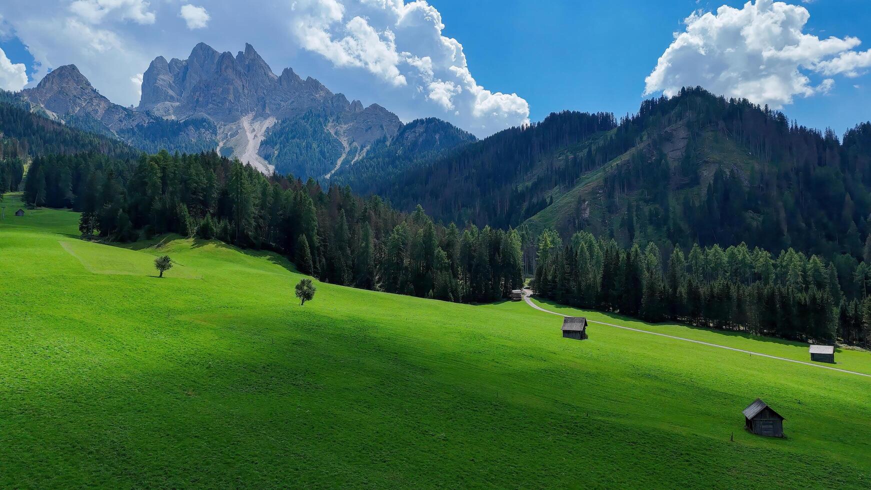 Majestic mountain landscape with lush green fields and rustic cabins under a bright blue sky in the Dolomites photo