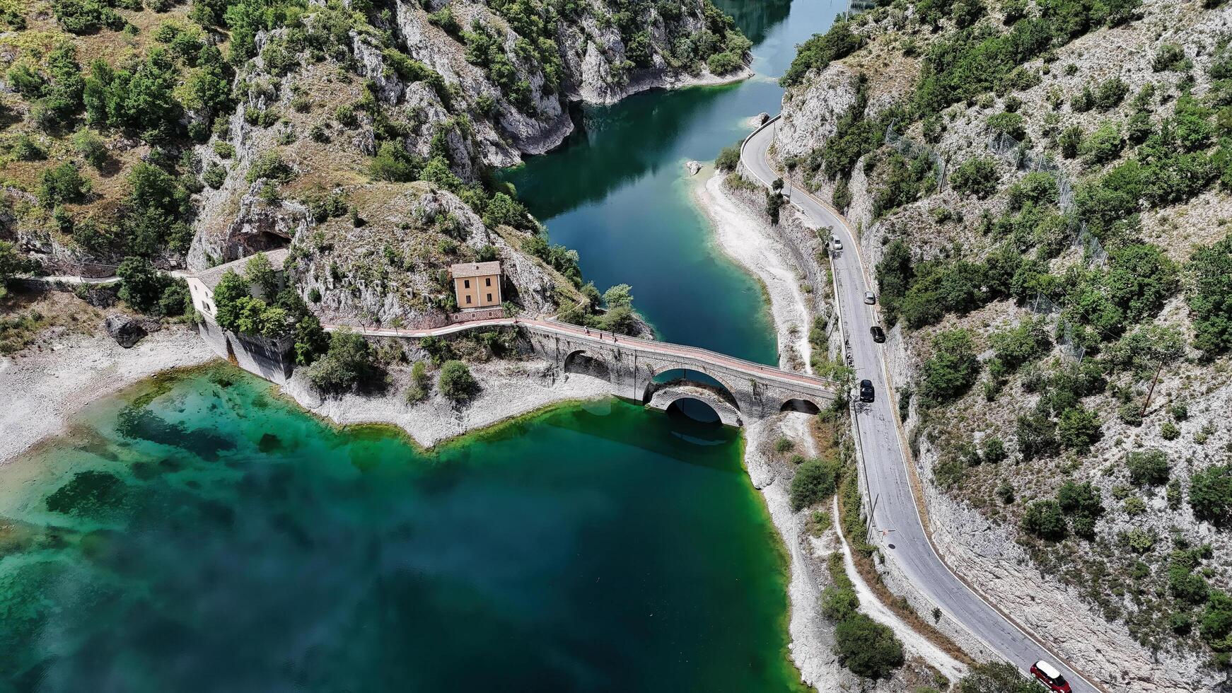 serene lake bordered by rocky hills and a charming bridge during a sunny day in nature photo