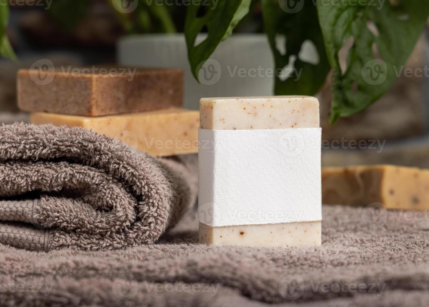 Soap bar with a label on brown folded towels near green plant in bathroom, mockup photo
