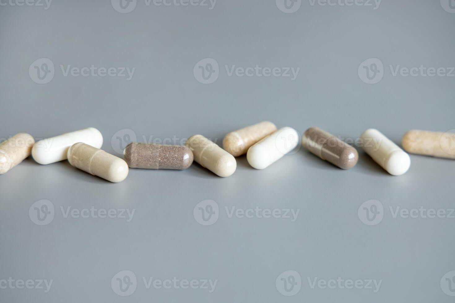 Mix of beige and brown medical capsules in a line on grey closeup. Dietary supplements and vitamins photo