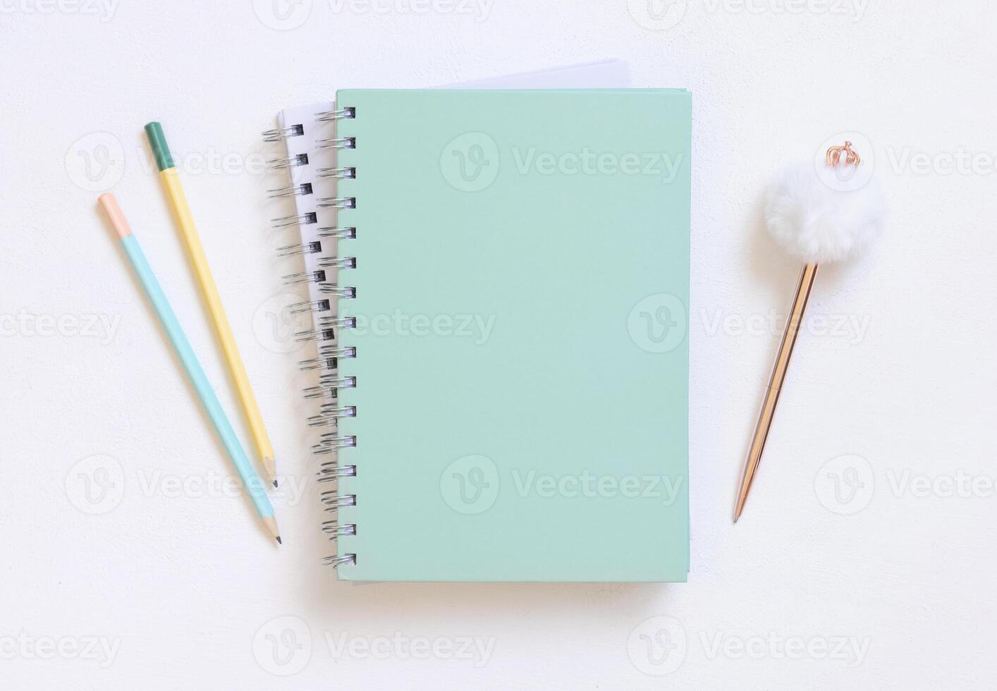 Blank spiral notebook on a white table near fur pen and pensils, school mockup photo