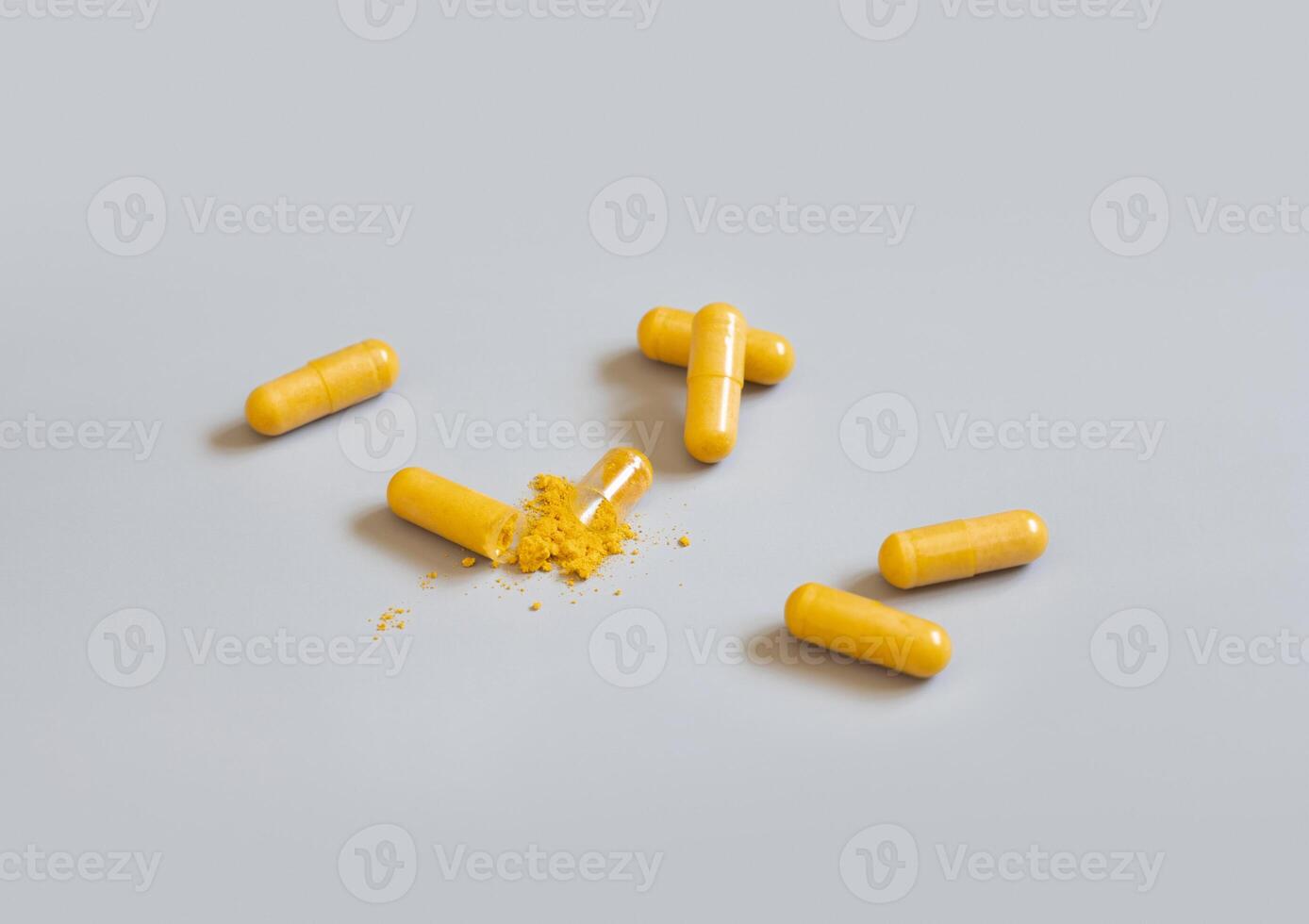 Opened Medical capsule to show yellow powder on grey top view. Dietary supplements photo