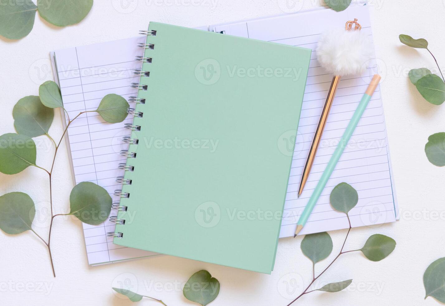 Blank spiral notebook on a white table near green eucalyptus leaves and pen, school mockup photo
