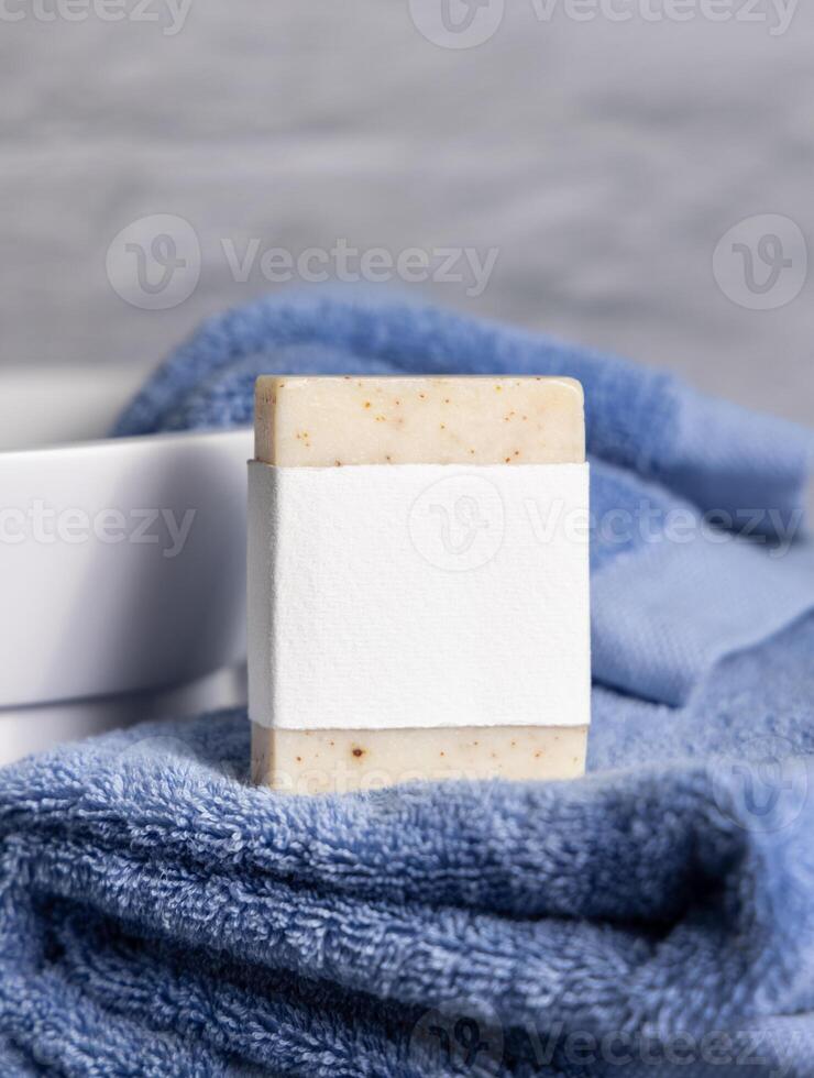 Soap bar with blank label on blue towels near sink in bathroom closeup, mockup photo