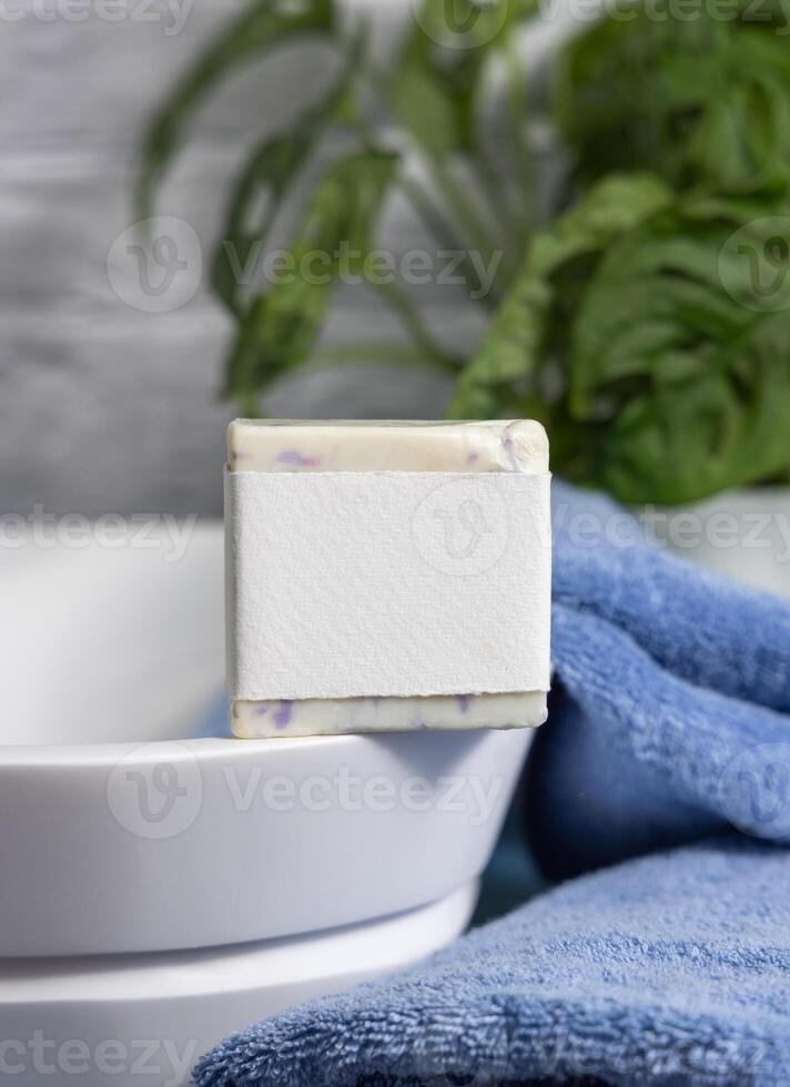 Soap with blank label on vessel sink near blue towels and green plant close up, mockup photo