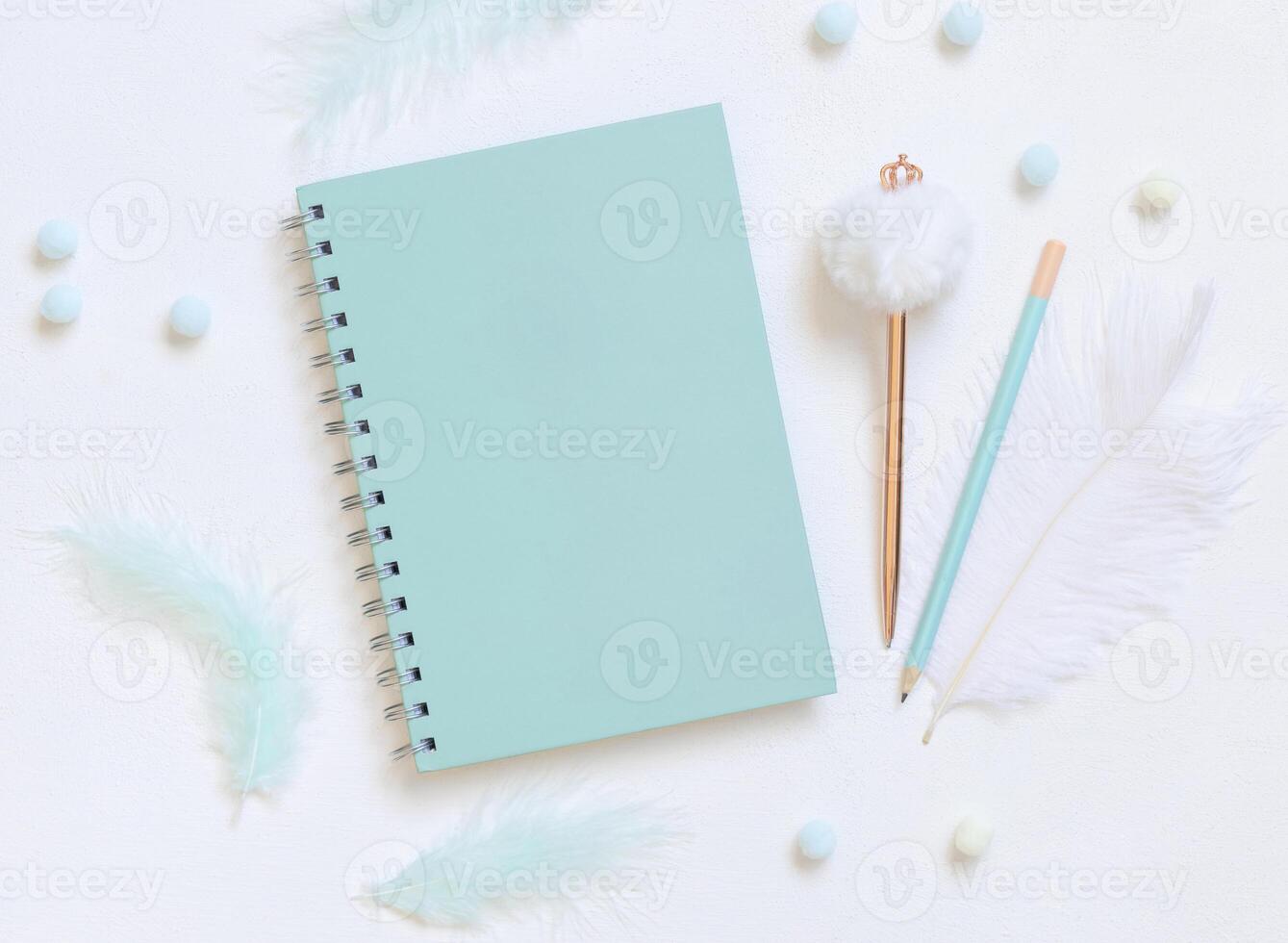 Blank spiral notebook on a white table near pastel feathers, pensil and fur pen, school mockup photo