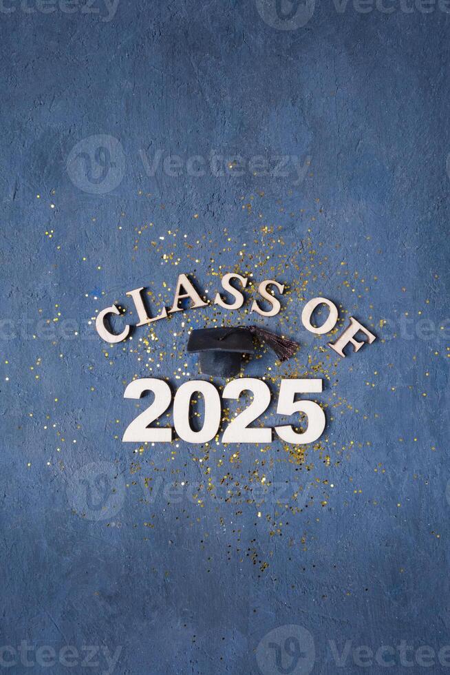 Graduation cap on wooden number 2025 on dark background with tinsel photo