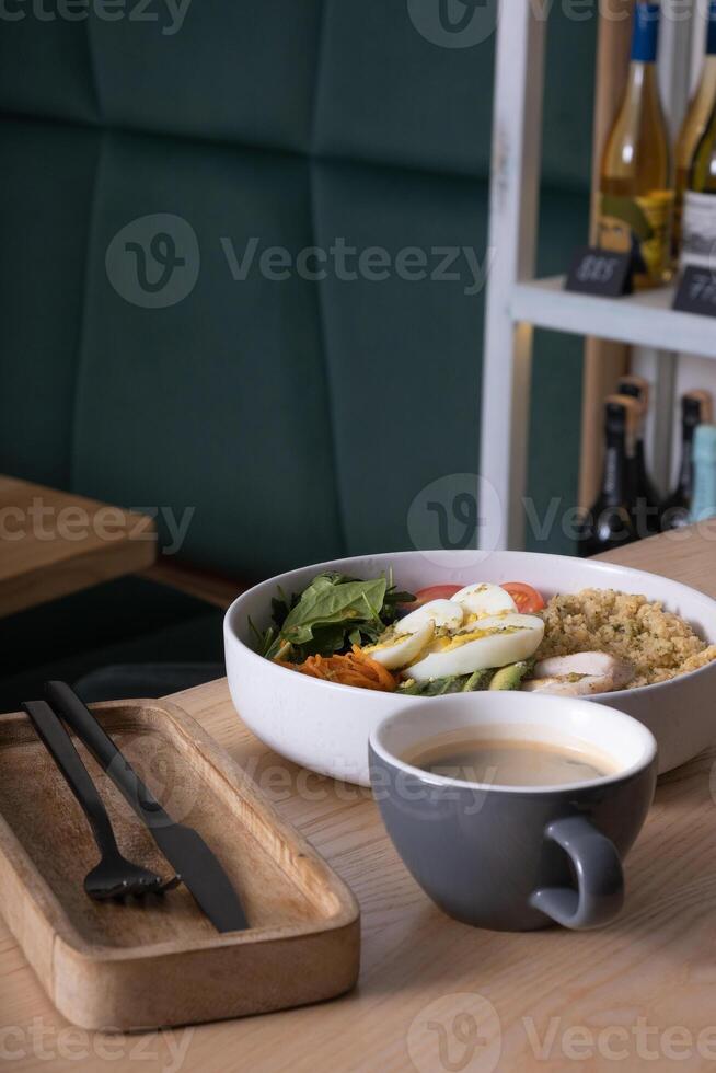 Plate with meat, eggs and avocado and vegetables and cup of coffee on cafe table photo