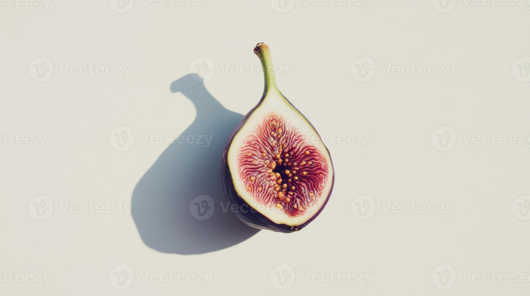 Half fresh fig sliced, casting dramatic shadow on white surface, revealing purple-red interior with golden seeds, embodying ripe fruit's delicate beauty and natural sweetness photo