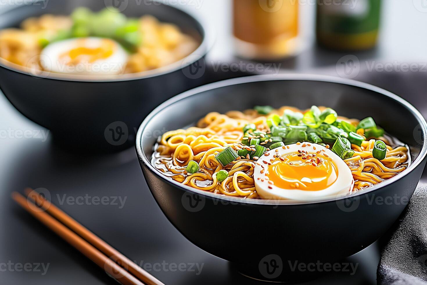 Two steaming bowls of ramen are presented on dark surface, complete with chopsticks photo