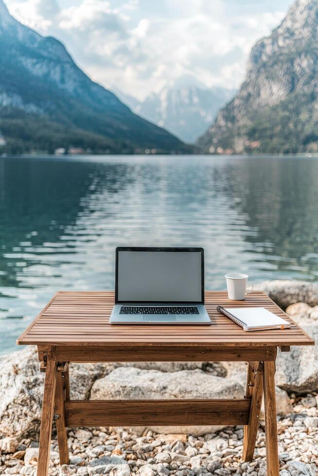 Desk with a laptop by a serene lake and mountains in the background. Work-life balance strategies concept. photo