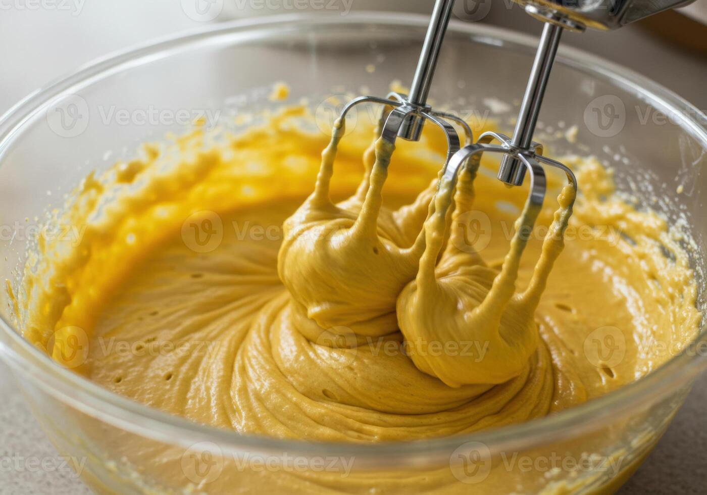 A hand mixer blending yellow cake batter in a glass bowl for baking. photo