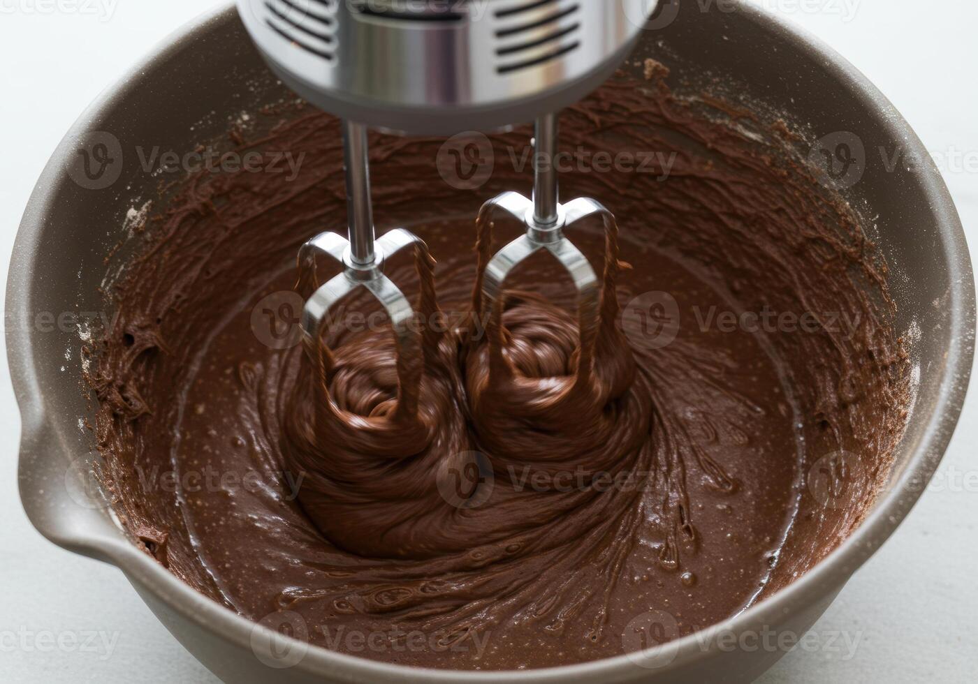Close up shot of an electric mixer blending chocolate batter inside a brown bowl. photo