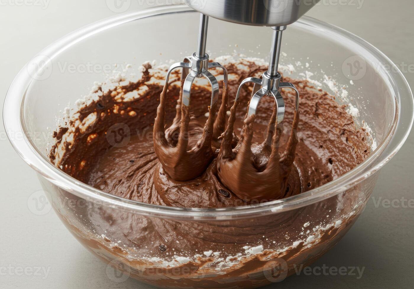 A close up of a clear bowl with chocolate batter being mixed with an electric mixer. photo