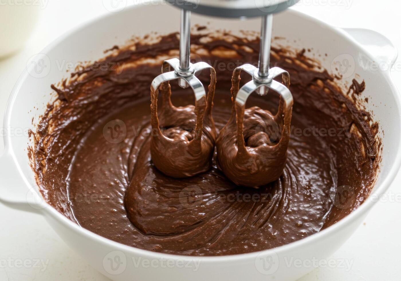 A close-up view of a mixer blending chocolate cake batter in a white bowl. photo