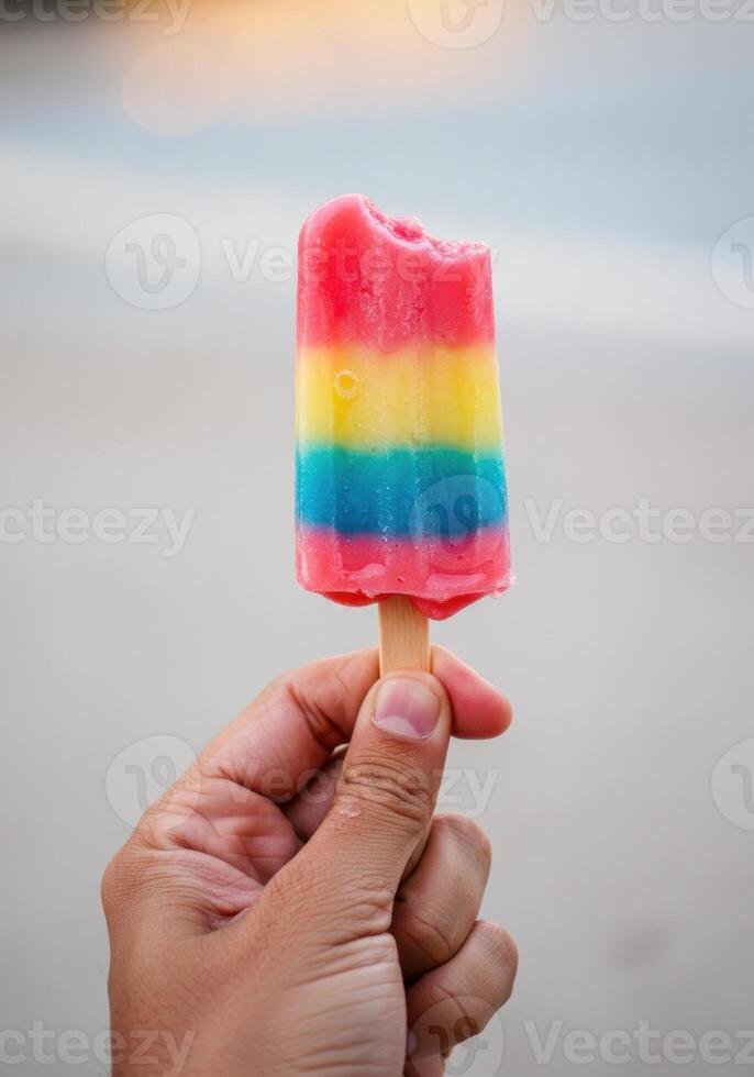 A refreshing, colorful popsicle with a bite taken out of it, held up in hand. photo